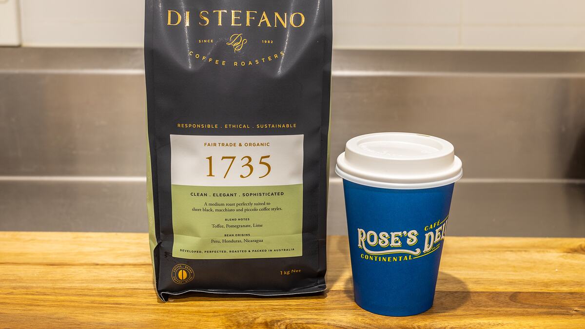 A Rose's Deli takeaway coffee cup beside a bag of Di Stefano 1735 coffee beans on the counter