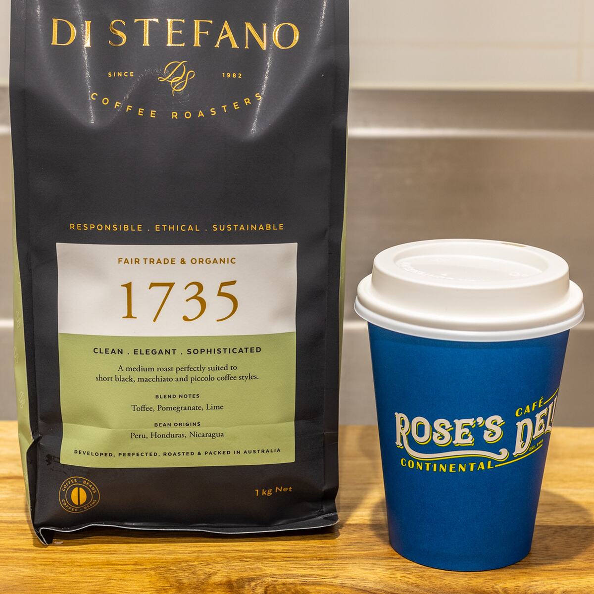 A Rose's Deli takeaway coffee cup beside a bag of Di Stefano 1735 coffee beans on the counter