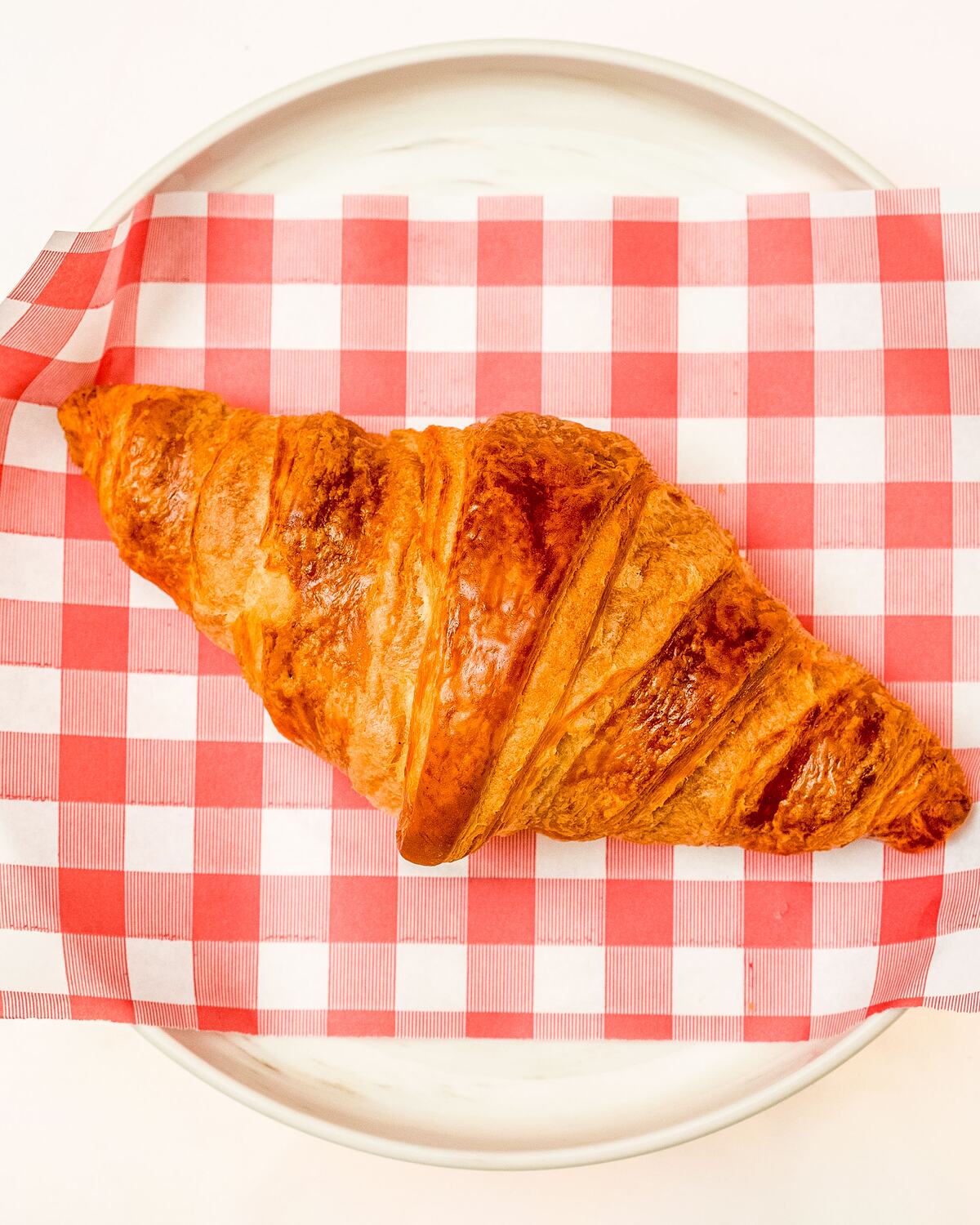 A golden croissant on a red gingham napkin