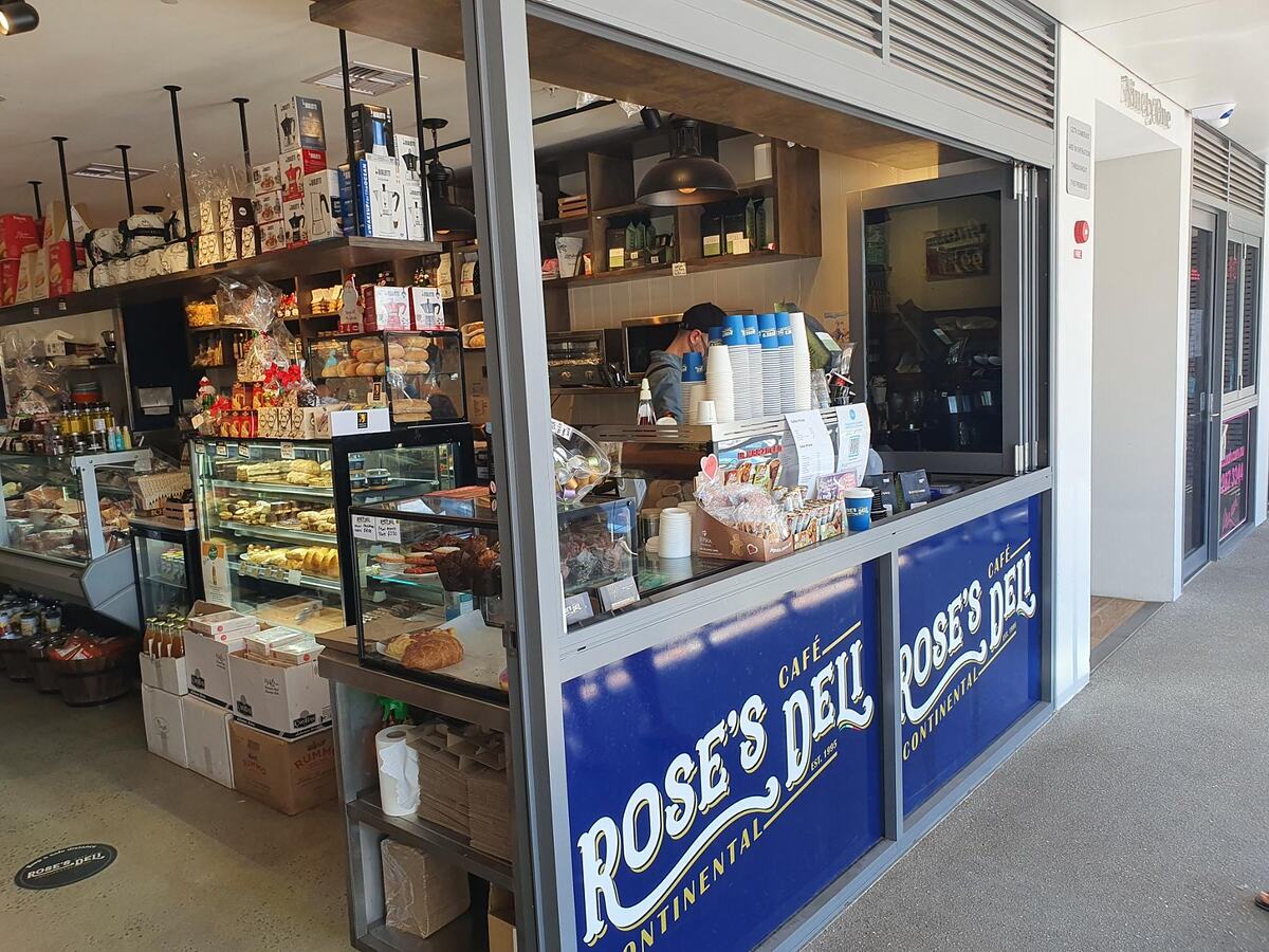 The Rose's Deli shopfront on McIntosh Road, Narraweena: navy Rose's Deli signs on the windows and the deli counter, cake cabinet and shelves of Italian groceries inside